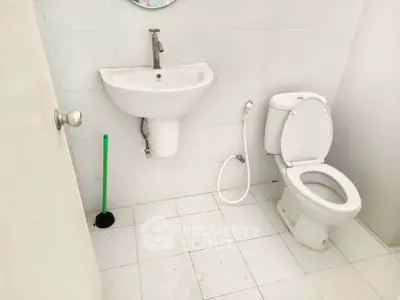 Compact bathroom with white fixtures and tiled floor, featuring a sink and toilet.
