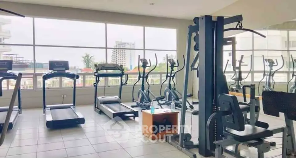 Spacious gym with modern equipment and large windows offering city views.