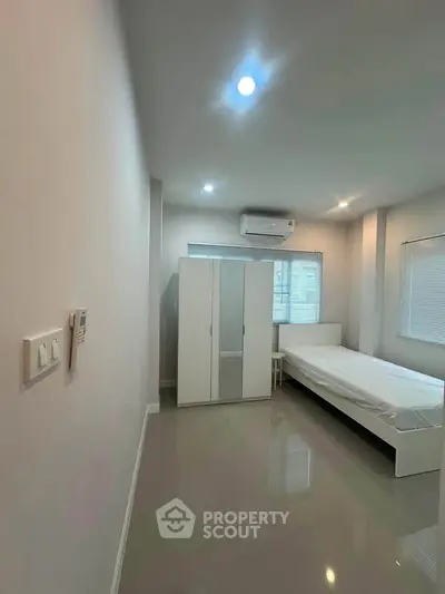 Minimalist bedroom with sleek white furniture and air conditioning, perfect for modern living.