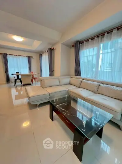Spacious living room with elegant white leather sectional and glass coffee table, featuring large windows and ample natural light.