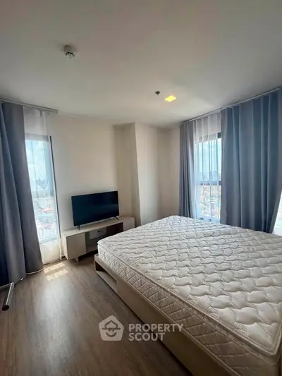 Spacious bedroom with large windows offering city views, featuring a comfortable bed and modern TV setup.