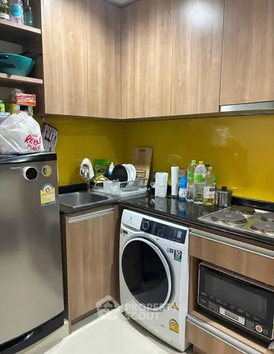 Modern kitchen with wooden cabinets, washing machine, and vibrant yellow backsplash.