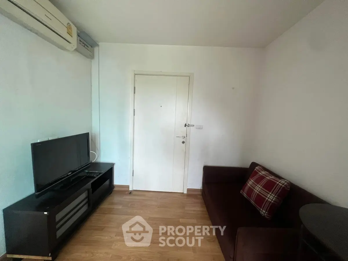 Cozy living room with TV and sofa, featuring wooden flooring and air conditioning.
