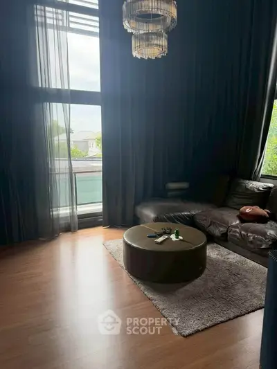 Luxurious living room with large windows and elegant chandelier, perfect for relaxation and entertaining.