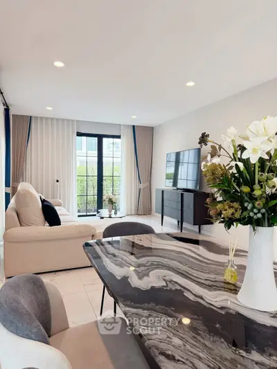 Elegant living room with modern decor, marble table, and large windows offering natural light.