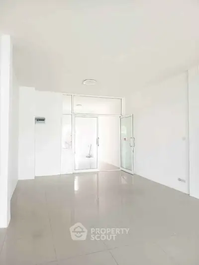 Spacious empty room with glossy tiled floor and glass door, ideal for office or retail space.
