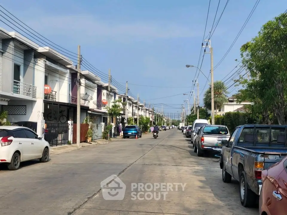 Charming residential street with modern townhouses and parked cars under a clear blue sky.
