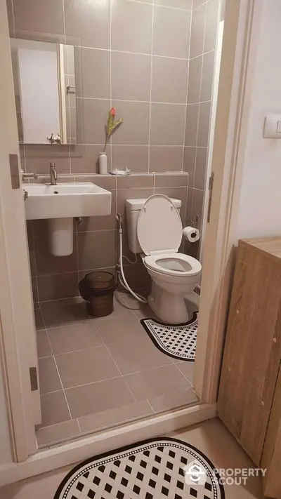 Modern bathroom with sleek design and neutral tiles, featuring a white sink and toilet.