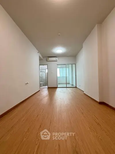 Spacious empty room with wooden flooring and glass sliding doors leading to a balcony.