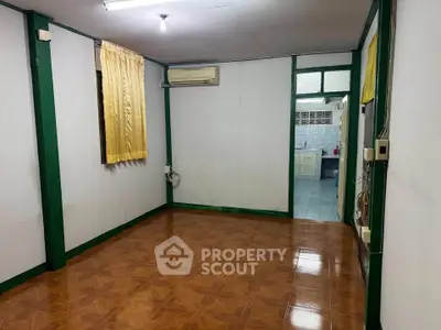 Spacious room with tiled flooring and air conditioning, leading to a kitchen area.