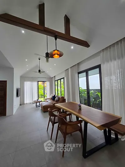 Spacious modern living room with high ceilings and elegant wooden beams, featuring large windows and stylish furniture.