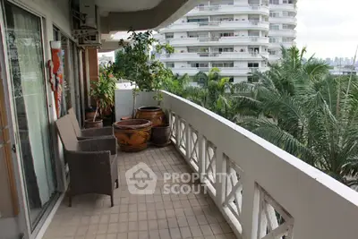 Spacious balcony with outdoor seating and lush greenery view in modern apartment complex.