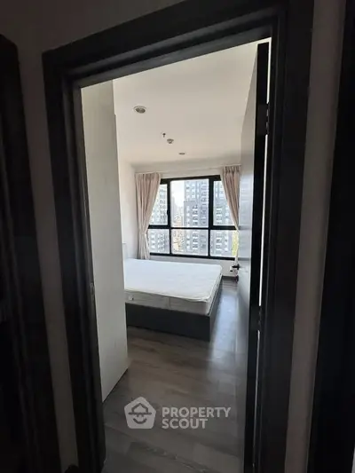 Modern bedroom with large windows and city view, featuring a minimalist design and natural light.