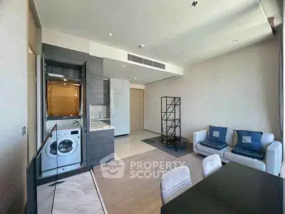 Modern living room with open kitchen and washing machine, featuring stylish furniture and ample natural light.