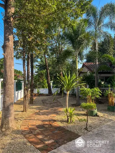 Charming garden pathway with lush greenery and tropical trees in a serene residential setting.