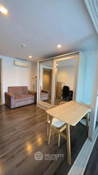 Modern living room with mirrored wardrobe and wooden desk, featuring sleek flooring and cozy seating.