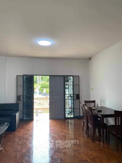 Spacious living room with wooden flooring and natural light, featuring a dining area and garden view.