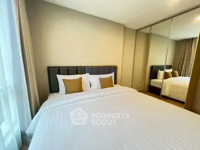 Spacious bedroom with mirrored closet and elegant bedding in modern apartment.