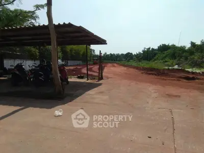 Spacious land plot with potential for development, featuring a covered parking area and lush greenery.