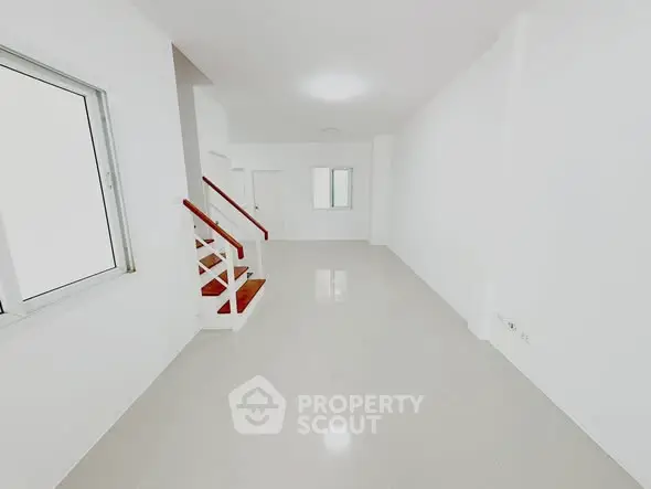 Spacious minimalist interior with sleek staircase and large window, perfect for modern living.