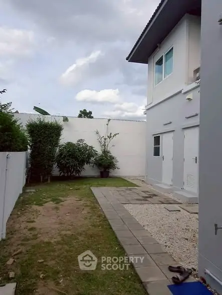 Charming backyard view of modern two-story home with lush greenery and paved walkway.
