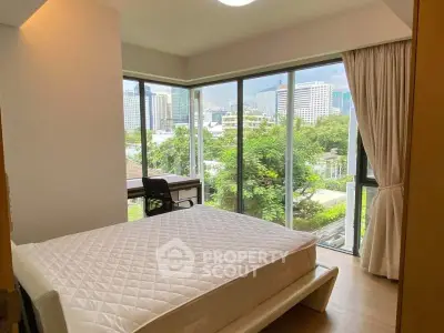 Spacious bedroom with large windows offering a stunning city view, featuring a comfortable bed and a study desk.