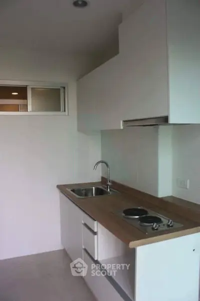 Modern compact kitchen with sleek cabinetry and electric cooktop in a minimalist apartment.