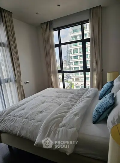 Modern bedroom with large window and city view, featuring elegant decor and cozy bedding.