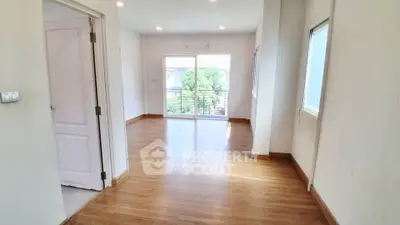 Spacious empty room with wooden flooring and large windows offering natural light.