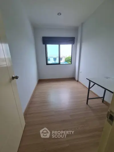 Spacious empty room with wooden flooring and large window, perfect for customization.