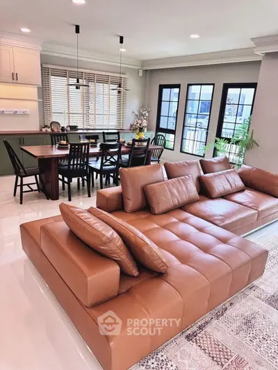Spacious living room with elegant leather sofa and dining area, featuring large windows and modern decor.