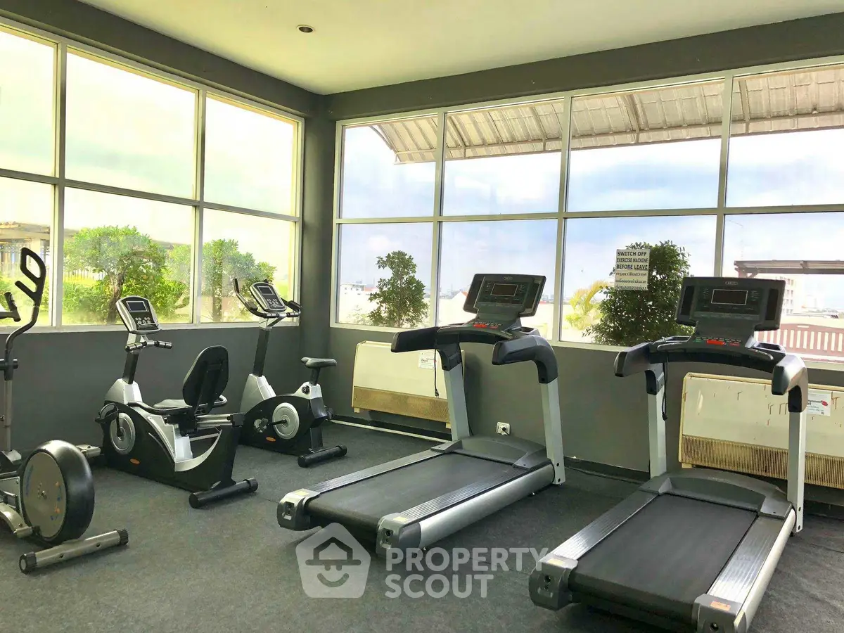 Spacious gym with modern exercise equipment and large windows offering natural light.