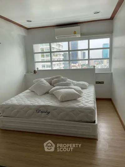 Cozy bedroom with city view, featuring a comfortable bed and large windows.