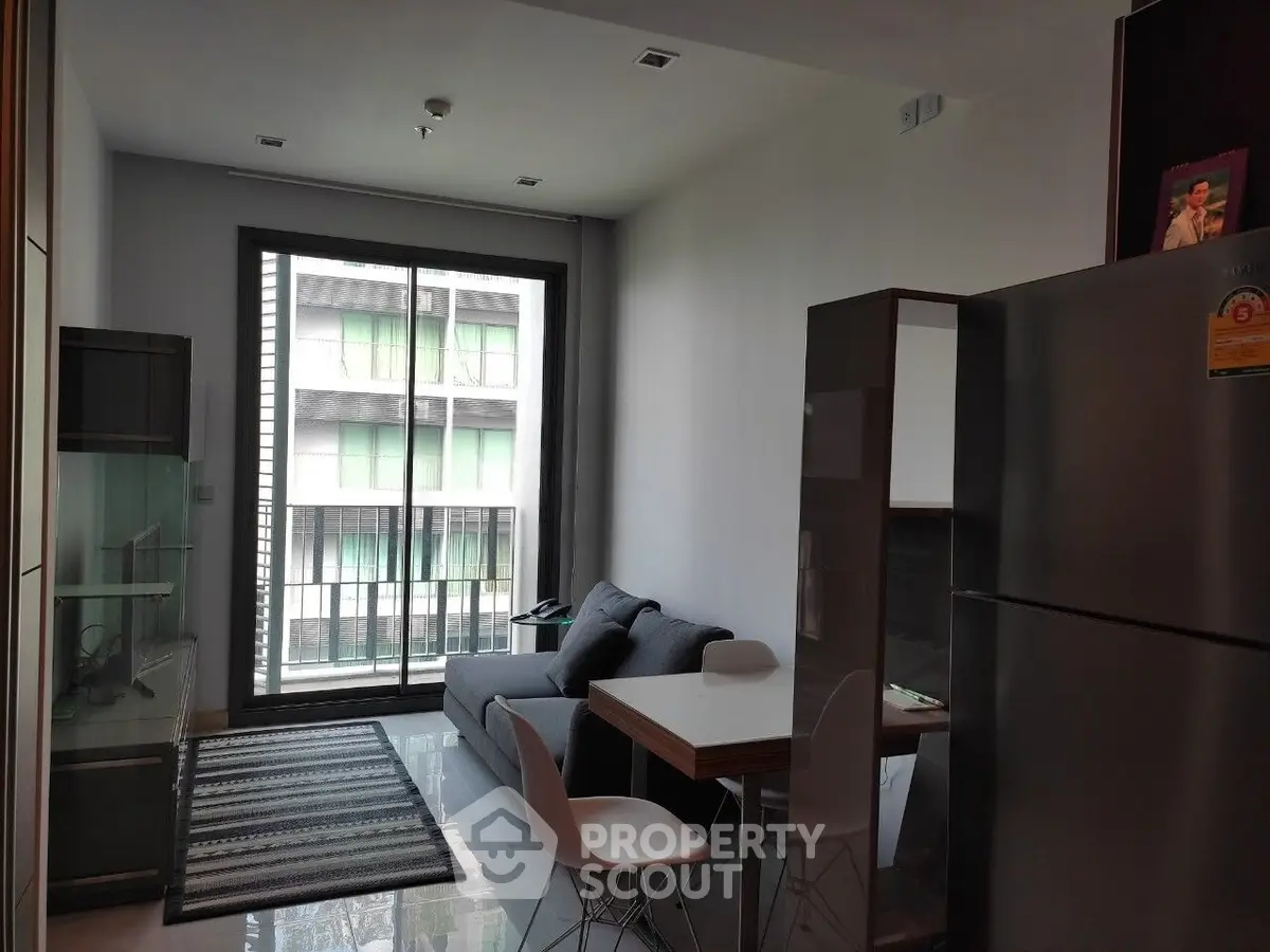 Modern living room with sleek furniture and large window offering natural light and urban view.