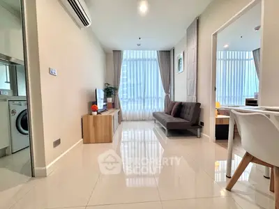 Modern living room with sleek furniture and natural light, adjacent to a compact kitchen area.
