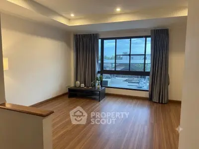 Spacious living room with large window and wooden flooring, offering a serene view.