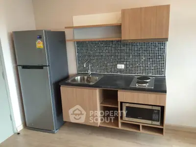 Modern compact kitchen with sleek cabinetry, stainless steel fridge, and built-in microwave in stylish apartment.