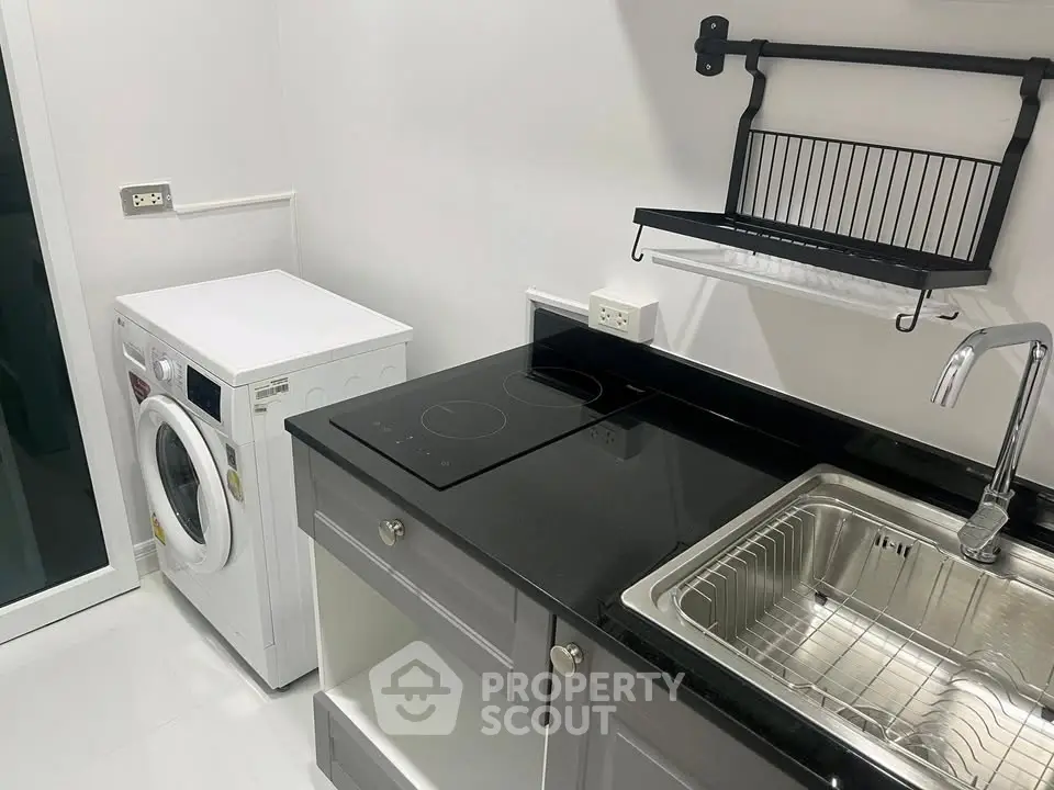 Modern kitchen with sleek black countertop and built-in appliances, featuring a washing machine and electric stove.