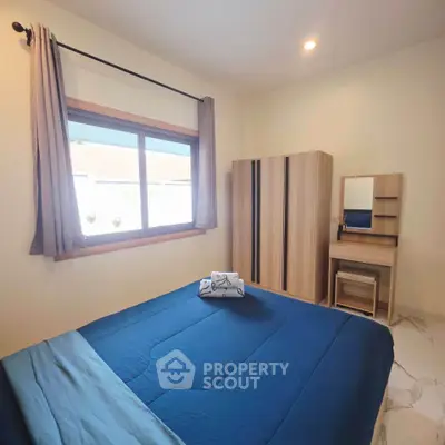 Cozy bedroom with blue bedding, wooden wardrobe, and natural light from window.