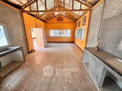 Spacious open-plan living area with bright orange walls and tiled flooring, featuring large windows for natural light.