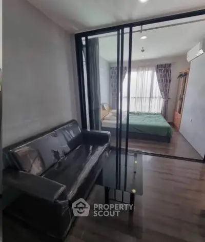 Modern apartment with glass partition separating living room and bedroom, featuring sleek furniture.