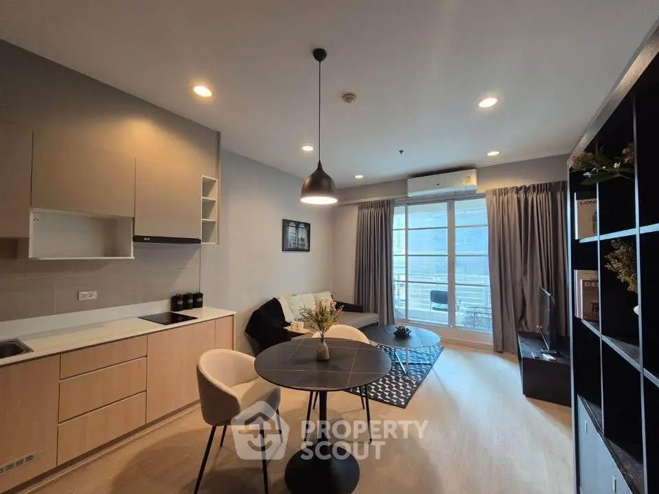 Modern living room with open kitchen and balcony view, featuring stylish furniture and natural light.