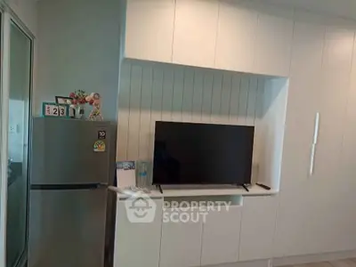 Modern kitchen with sleek cabinetry and integrated TV setup, featuring a stainless steel fridge.
