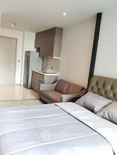 Modern studio apartment with cozy bed and compact kitchen area, perfect for urban living.