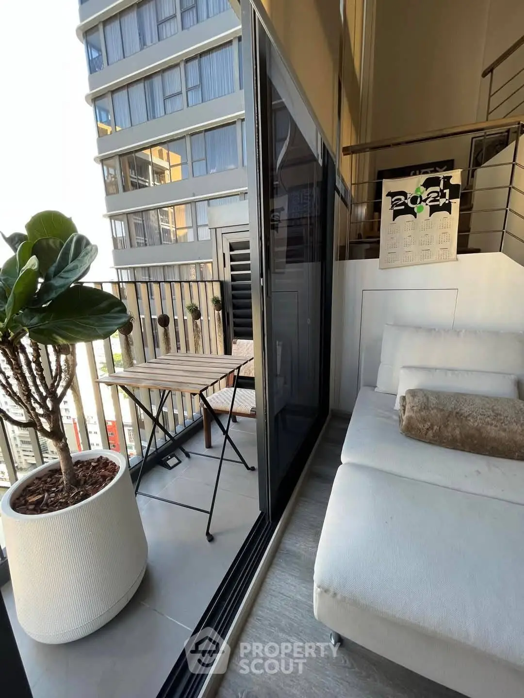 Modern balcony with cozy seating and potted plant in urban high-rise apartment.