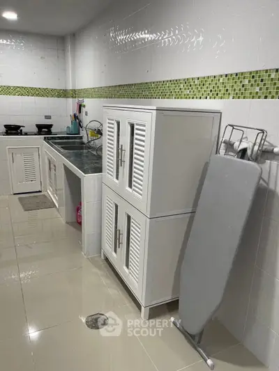 Modern kitchen with sleek cabinets and ironing board, featuring a tiled backsplash and glossy floor.
