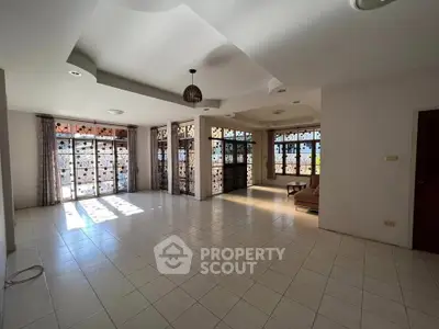 Spacious living room with large windows and tiled flooring, perfect for natural light and comfort.