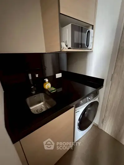 Compact kitchen with modern appliances including a washing machine and microwave, sleek black countertop.