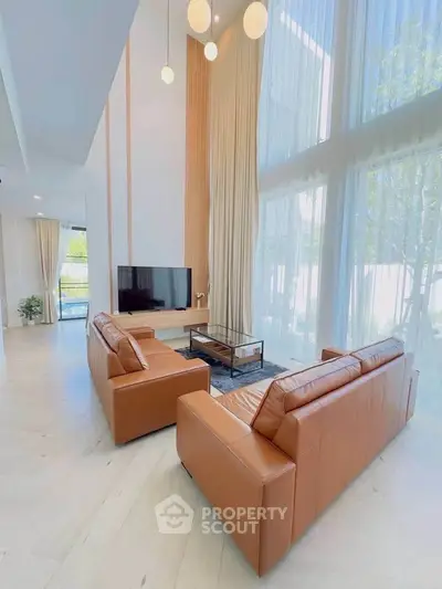 Luxurious living room with high ceilings, leather sofas, and large windows for natural light.