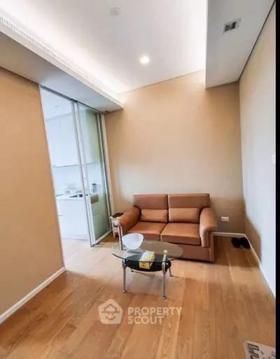 Cozy living room with modern sofa and glass coffee table, adjacent to a sleek kitchen area.